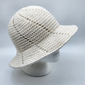 May include: A white crocheted sun hat with a wide brim. The hat is made with a simple stitch pattern and has a slightly slouchy fit.