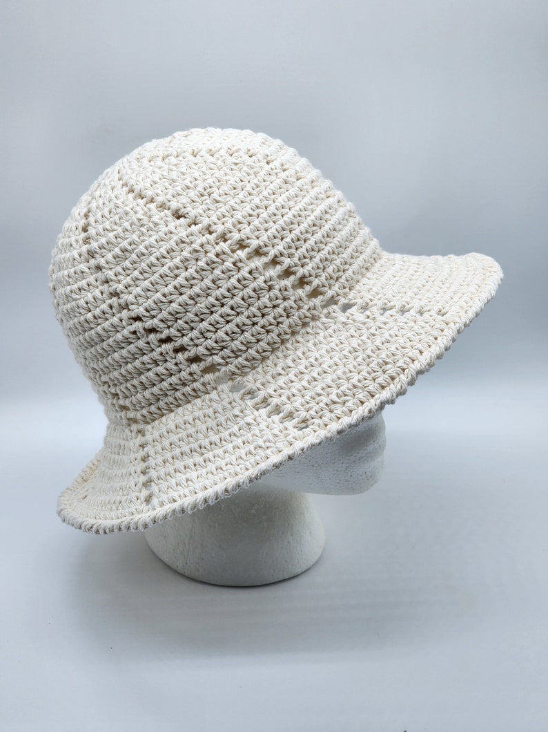 May include: A white crocheted sun hat with a wide brim. The hat is made with a simple stitch pattern and has a slightly slouchy fit.