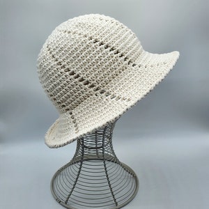 May include: A white crocheted sun hat with a wide brim and an open weave pattern. The hat is displayed on a wire hat stand.