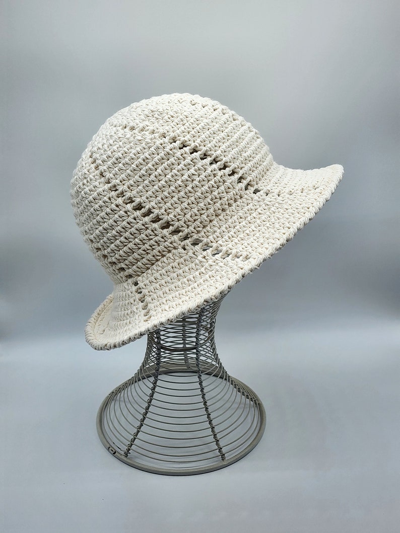 May include: A white crocheted sun hat with a wide brim and an open weave pattern. The hat is displayed on a wire hat stand.