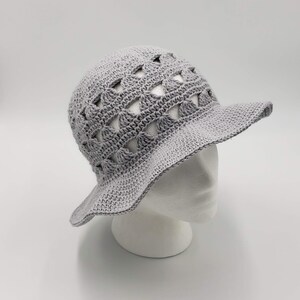 May include: A grey crocheted sun hat with a wide brim and a geometric pattern. The hat is made with open stitches, creating a lightweight and airy design.