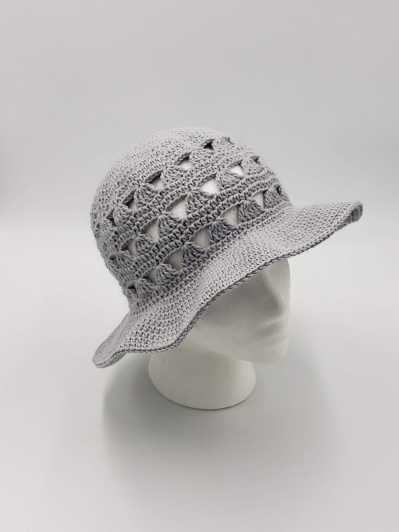 May include: A grey crocheted sun hat with a wide brim and a geometric pattern. The hat is made with open stitches, creating a lightweight and airy design.