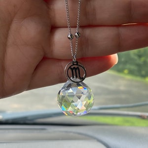 May include: A silver chain necklace with a crystal ball pendant and a small charm with the astrological symbol for Scorpio.