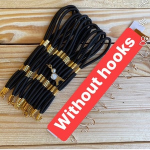 以下が含まれることがあります： 金色のアクセントが付いた黒いヘアゴム15個のセット。ヘアゴムは積み重ねられており、そのうちの1つには小さな金色のチャームが付いています。チャームはエッフェル塔のデザインです。赤と白の看板には「フックなし」と書いてあります。