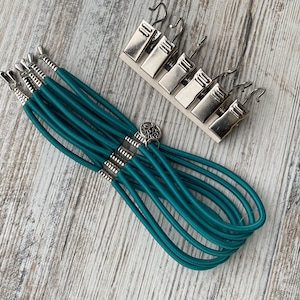 May include: Teal elastic cord with silver metal accents and a decorative charm. The cord is bundled together and appears to be a bracelet or necklace.