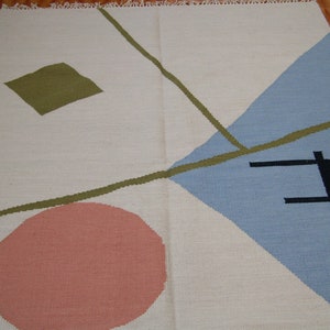 May include: A white rug with geometric shapes in green, blue, and pink. The rug has a diamond shape in the top left corner, a circle in the bottom left corner, and a triangle in the top right corner.