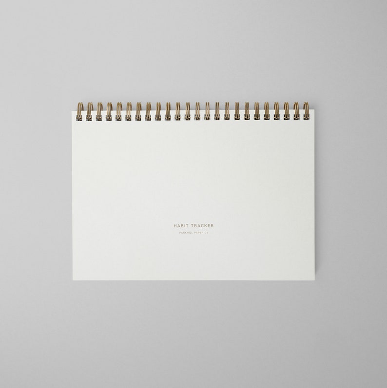 K&ouml;nnte beinhalten: Ein wei&szlig;es Notizbuch mit Spiralbindung und dem Text "HABIT TRACKER" auf dem Einband.