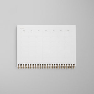 K&ouml;nnte beinhalten: Ein wei&szlig;er Monatskalender mit einer goldenen Spiralbindung. Der Kalender hat ein schlichtes Design mit den Wochentagen, die oben beschriftet sind.