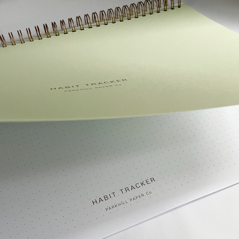 K&ouml;nnte beinhalten: Ein hellgr&uuml;nes Notizbuch mit einer goldenen Spiralbindung. Der Einband hat den Text "HABIT TRACKER PARKHILL PAPER CO." in Schwarz gedruckt. Der hintere Einband ist wei&szlig; mit einem gepunkteten Muster und dem Text "HABIT TRACKER PARKHILL PAPER CO." in Schwarz gedruckt.