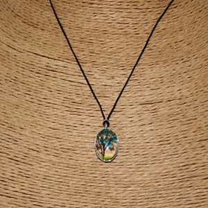 May include: A black cord necklace with a silver oval pendant featuring a colorful tree painting inside.