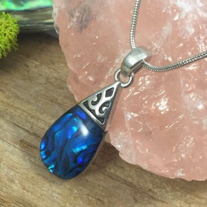 May include: A silver chain necklace with a blue abalone shell pendant. The pendant is shaped like a teardrop and has a silver filigree design around the edge.