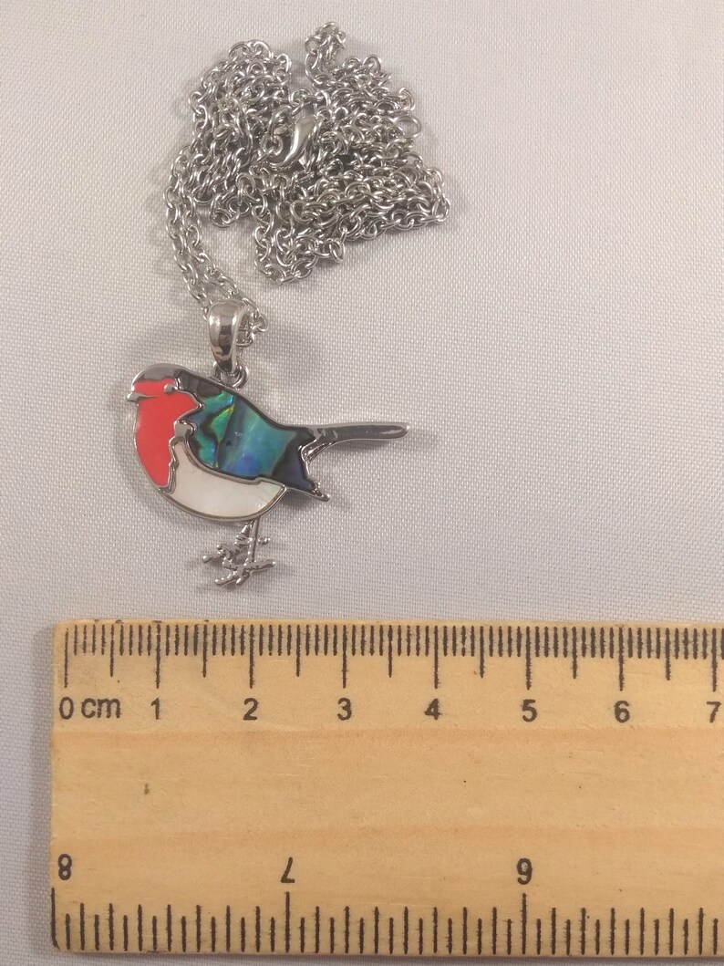 May include: A silver-toned bird pendant necklace. The bird has a red breast, white belly, and iridescent blue and green wing. The necklace chain is also silver. The pendant is approximately 1.5 inches long.