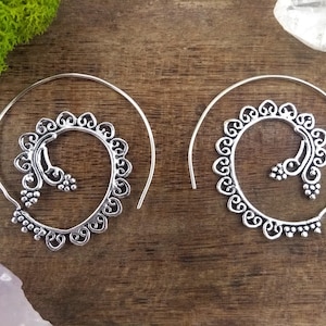 May include: A pair of silver hoop earrings with a delicate, intricate design. The earrings are made of thin wire and have a spiral shape.