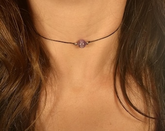 May include: A simple choker necklace with a single, round, purple gemstone bead.