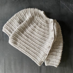 Może przedstawiać: Szary kardigan wykonany na szydełku z guzikami.