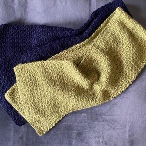 Peut inclure: Deux écharpes en crochet, l'une en bleu foncé et l'autre en vert clair, sont pliées et posées sur une surface grise.