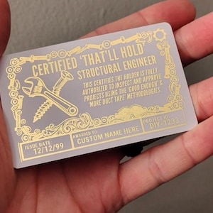 May include: A clear plastic card with gold text and graphics. The card reads "CERTIFIED 'THAT'LL HOLD' STRUCTURAL ENGINEER" with a wrench and screw graphic. It includes the text "AWARDED TO CUSTOM NAME HERE" and "PROJECT ID DIY-1233".