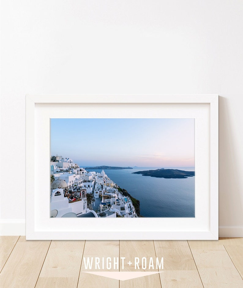 Coastal decor featuring a blue sunset in Santorini Greece. This photograph shows the aegean sea and caldera views in the background and white city buildings of Fira in the foreground.