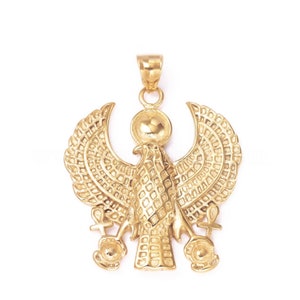 May include: Gold pendant featuring a detailed design of an Egyptian goddess with outstretched wings, holding an ankh symbol in each hand.