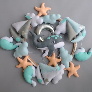 Puede incluir: Un m&oacute;vil para beb&eacute; con una ballena, nubes, veleros y estrellas de mar. El m&oacute;vil est&aacute; hecho de fieltro y tiene un anillo de madera.