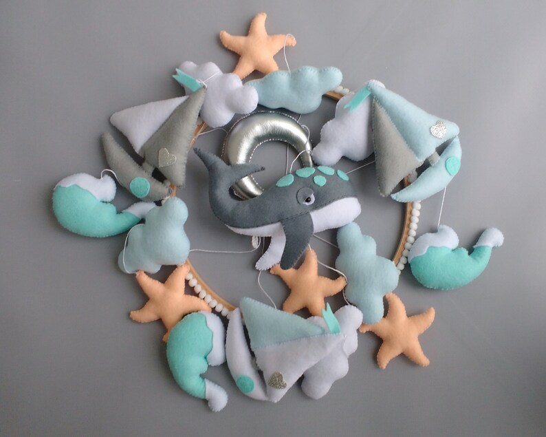 Puede incluir: Un m&oacute;vil para beb&eacute; con una ballena, nubes, veleros y estrellas de mar. El m&oacute;vil est&aacute; hecho de fieltro y tiene un anillo de madera.