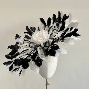 May include: A black and white feather headpiece with a single white flower. The headpiece is displayed on a white mannequin head.