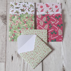 May include: A set of Christmas-themed envelopes with various designs. The envelopes are red, green and white with holly, candy canes and Christmas trees. One envelope is open to show the white interior.