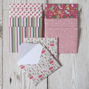 May include: A set of Christmas themed envelopes with various patterns, including red and green stripes, candy canes, and Santa Claus. The envelopes are on a light wood background.