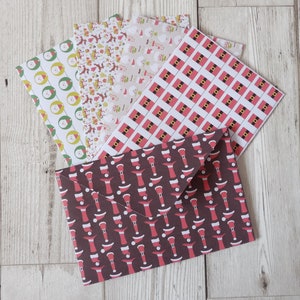May include: A set of five Christmas-themed envelopes with different patterns. The envelopes are white with red and green designs, including Santa hats, reindeer, and snowflakes. The envelopes are folded and stacked on top of each other.