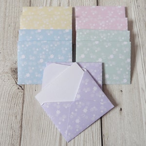 May include: A set of 10 blank note cards with envelopes. The envelopes are in four colours: yellow, light blue, light green, and lavender. Each envelope has a white floral pattern.