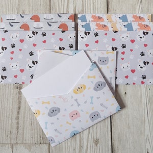 May include: A set of six envelopes featuring different animal print designs. The envelopes are white with a variety of colourful animals, including cats, dogs, and fish. The envelopes are all folded and stacked on top of each other.