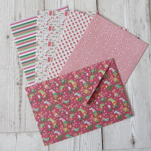 May include: A set of five Christmas-themed envelopes with different patterns. The envelopes are pink, red and white with designs of candy canes, elves and snowflakes.