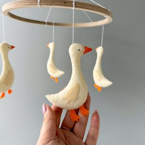 May include: A wooden ring mobile with four white felt geese hanging from it. The geese have orange felt feet and beaks.