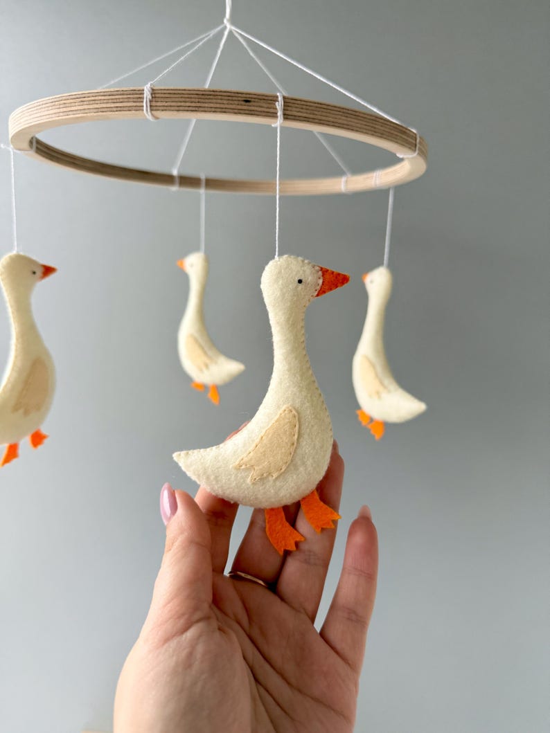 May include: A wooden ring mobile with four white felt geese hanging from it. The geese have orange felt feet and beaks.