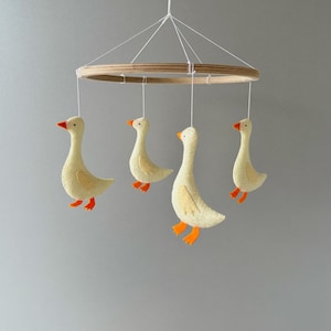 May include: A wooden ring mobile with four felt geese hanging from it. The geese are yellow with orange beaks and feet.