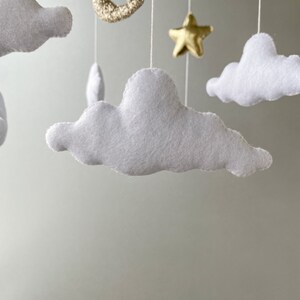 May include: A white felt cloud mobile with gold glitter stars and a crescent moon hanging from a white string.