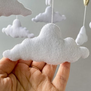 May include: A white felt cloud mobile with multiple clouds hanging from a string. The clouds are soft and fluffy, and they are perfect for a baby's nursery.