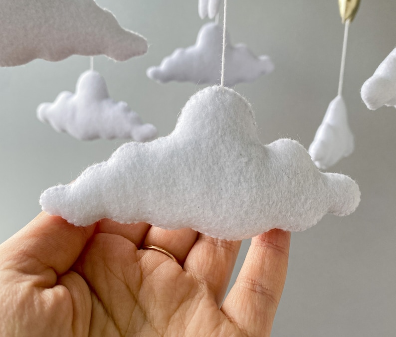 May include: A white felt cloud mobile with multiple clouds hanging from a string. The clouds are soft and fluffy, and they are perfect for a baby's nursery.