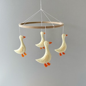 May include: A wooden baby mobile with four felt geese hanging from it. The geese are yellow with orange beaks and feet.