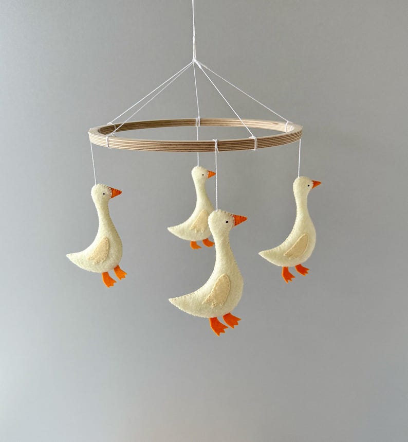 May include: A wooden baby mobile with four felt geese hanging from it. The geese are yellow with orange beaks and feet.