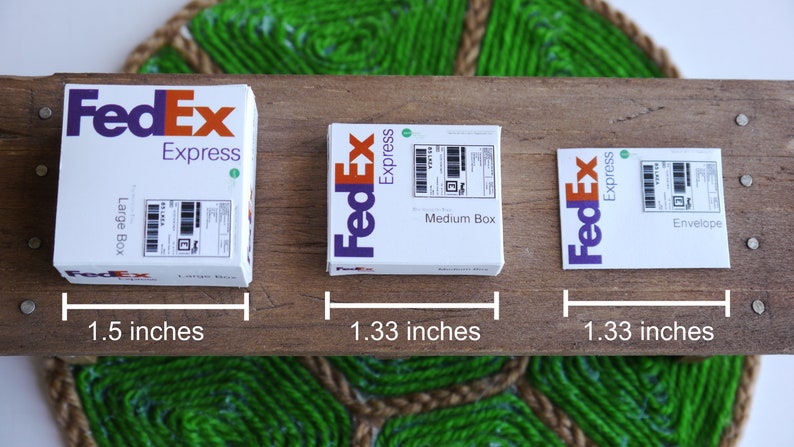 以下が含まれることがあります： 異なるサイズのFedExの配送箱が3つあります。一番大きな箱には「Large Box」、中くらいの箱には「Medium Box」、一番小さな箱には「Envelope」とラベルが貼られています。箱は木製の表面に並べてあり、インチで測定されています。