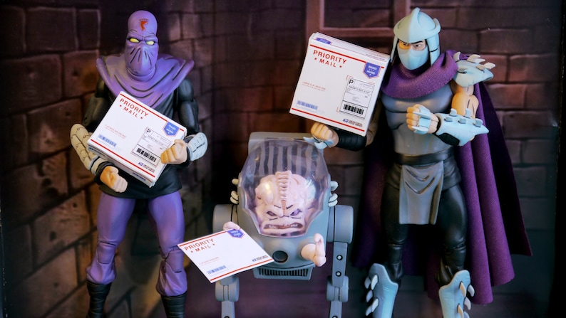 May include: Action figures of characters from the Teenage Mutant Ninja Turtles franchise. The figures are holding white boxes with "PRIORITY MAIL" printed on them. The figures are in a room with a brick wall.