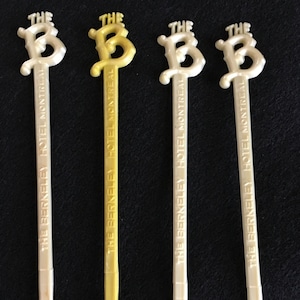 May include: Four white plastic spoons with gold lettering. The spoons have the words "The Berkeley Hotel Montreal" printed on them.