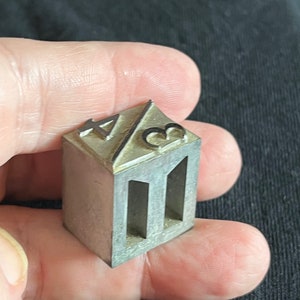 May include: A silver metal stamp with the numbers 1 and 3 on the top and two rectangular cutouts on the front.