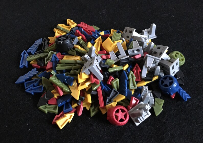May include: A pile of colorful plastic game pieces, including arrows, stars, and small figures. The pieces are in various shades of blue, green, yellow, red, and gray.