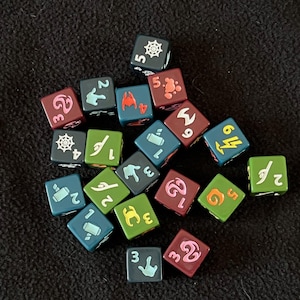 May include: A collection of colorful dice with various symbols and numbers. The dice are in shades of green, blue, and maroon, with white and orange symbols. The dice are scattered on a dark, textured surface, suitable for tabletop games.