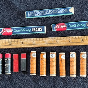 May include: Three rectangular boxes of Scripto Smooth Writing Leads, a wooden ruler measuring 10 inches, and ten cylindrical containers of lead refills. The containers are labeled Sharp, Pal Indelible Leads, and include two plain red and black blocks.