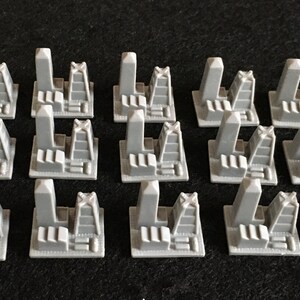 May include: Set of 18 gray plastic building pieces for a board game. Each piece features a tall tower with a cross on top and a smaller building with a flat roof.