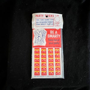 May include: A vintage party game called "Be a Smarty" with a red and white background. The game includes 3 games with 36 pull tabs. The game is designed for teenage and adult parties.