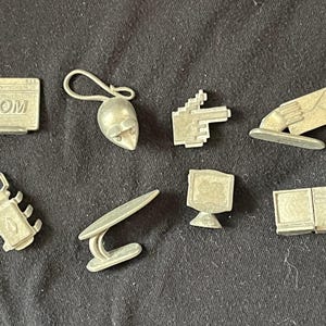 May include: A set of nine silver-colored game pieces featuring various computer-related icons, including a mouse, a hand pointing, a computer monitor, a floppy disk, a computer screen with the text '.com', a bug, and a hand holding an envelope.